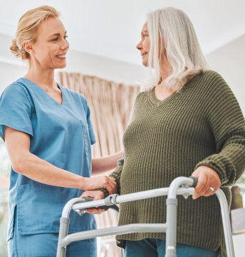 A female caregiver assisting a senior woman to walk