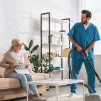 A male caregiver cleaning the room of a senior woman