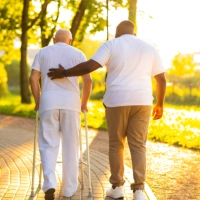 A male assisting a senior man to walk outside